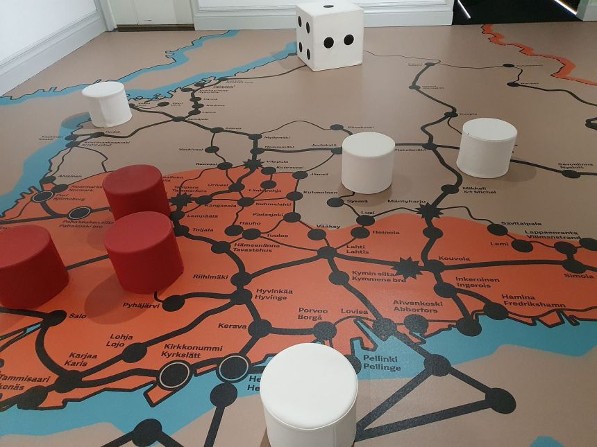 Johanna Lecklinin näyttelystä kuva, jossa huoneen lattialla toisinto sisällissodan aikaisesta lautapelistä. Kuvassa kartta, jonka päällä punaisia ja valkoisia nappuloita ja noppa.